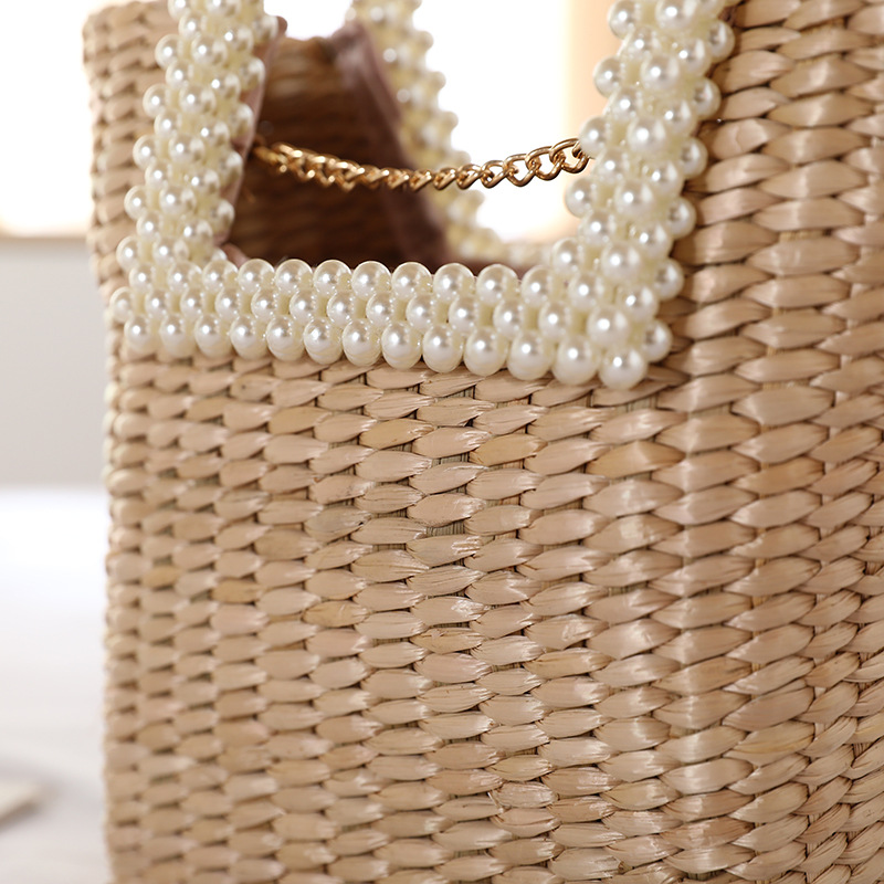 Close-up of pearl handle and gold chain on beige straw tote bag
