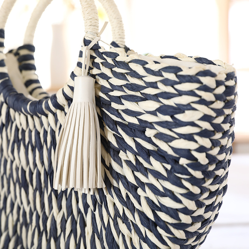 Close-up view of white tassel decoration on striped straw tote bag