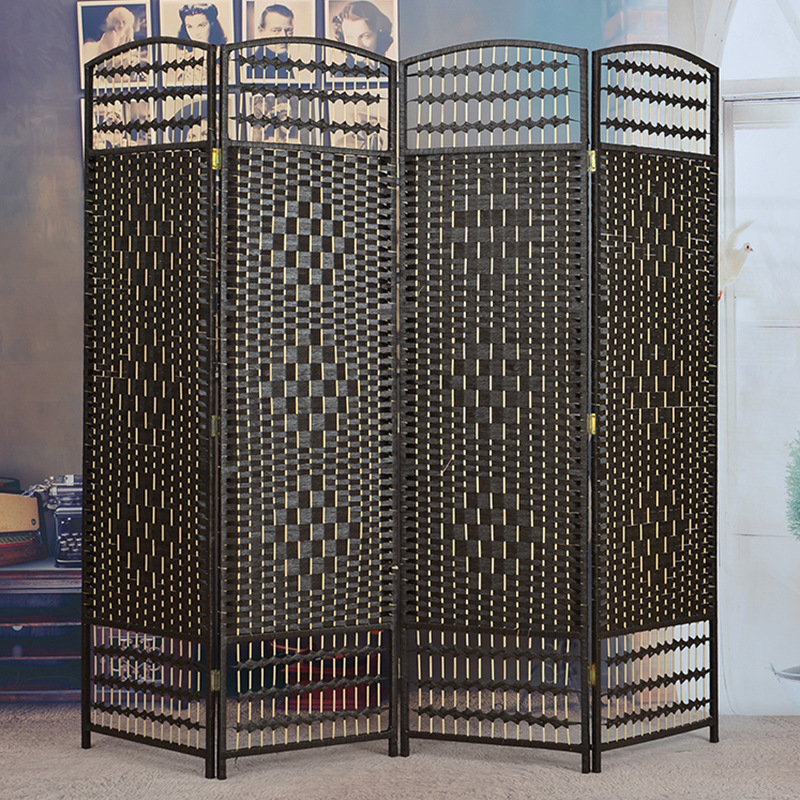 Black woven room divider in front of a vintage poster wall with a typewriter and a woven floor mat nearby
